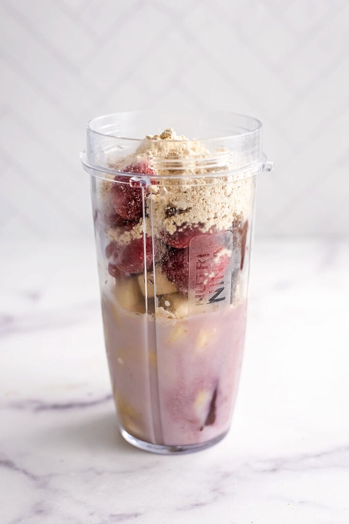 Strawberry banana acai bowl ingredients in a blender cup before being blended.