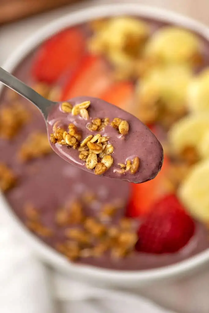 Strawberry banana smoothie bowl with a spoon full of smoothie and granola.
