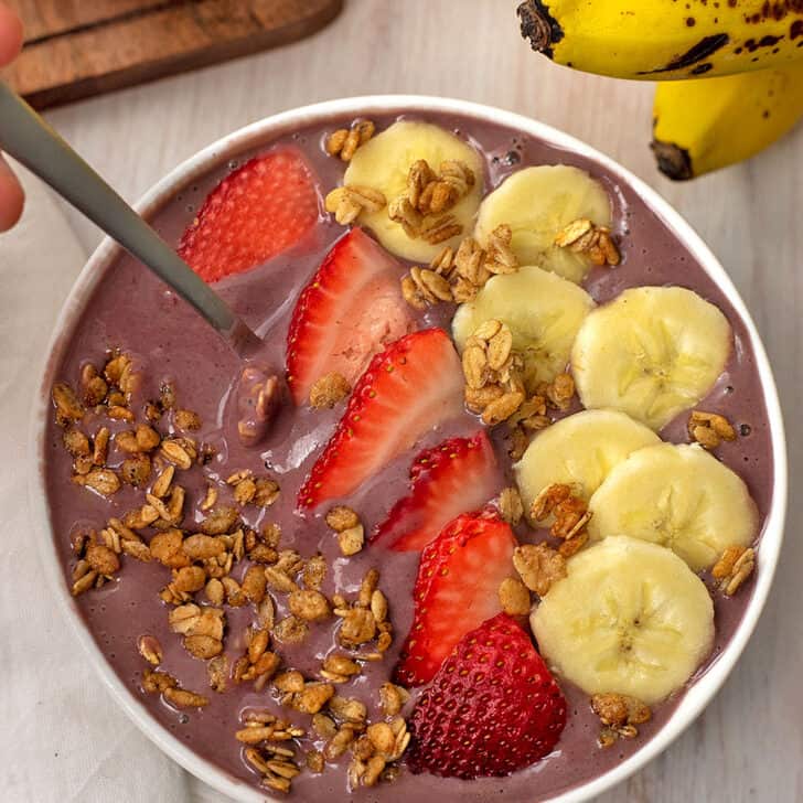 Strawberry banana smoothie bowl with a spoon. Banana and strawberry slices are on top along with granola.