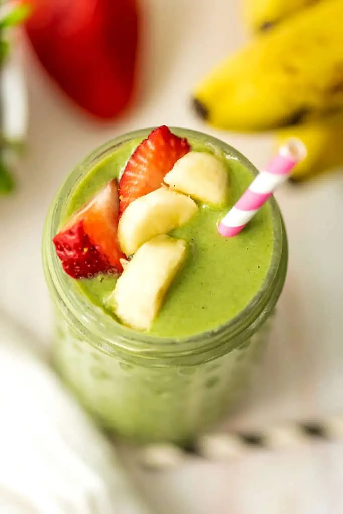 Strawberry banana spinach smoothie with sliced banana and strawberries on top.