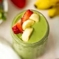 Strawberry banana spinach smoothie in a speckled glass with sliced fruit on top.