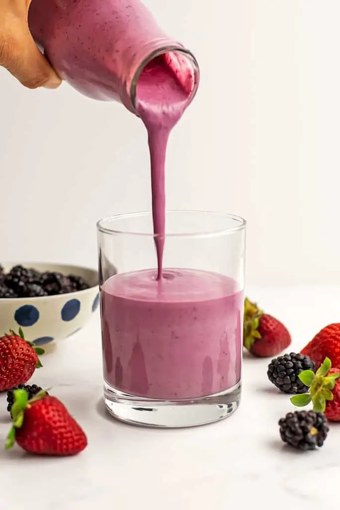 Strawberry blackberry smoothie being poured into a glass.