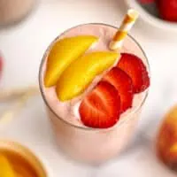 Strawberry peach smoothie in a glass with sliced strawberries on top.