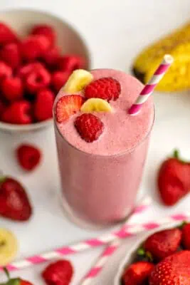 Strawberry raspberry banana smoothie with fruit on top and a straw.