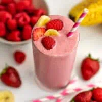 Strawberry raspberry banana smoothie in a glass with fruit on top.