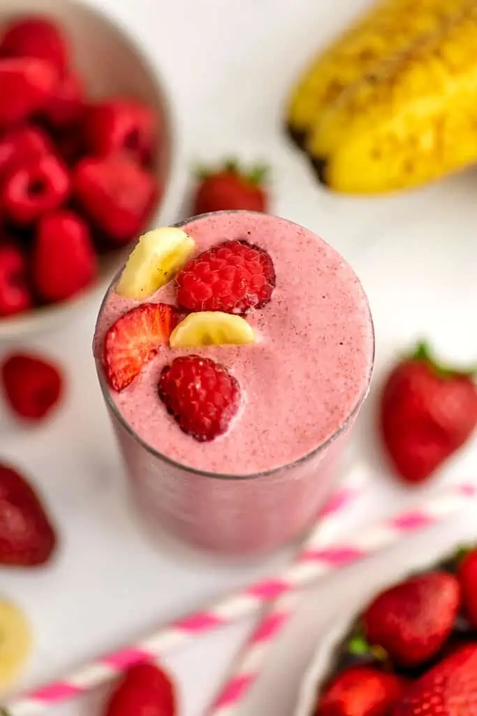 Overview of a strawberry raspberry banana smoothie with raspberries in a bowl in the background.