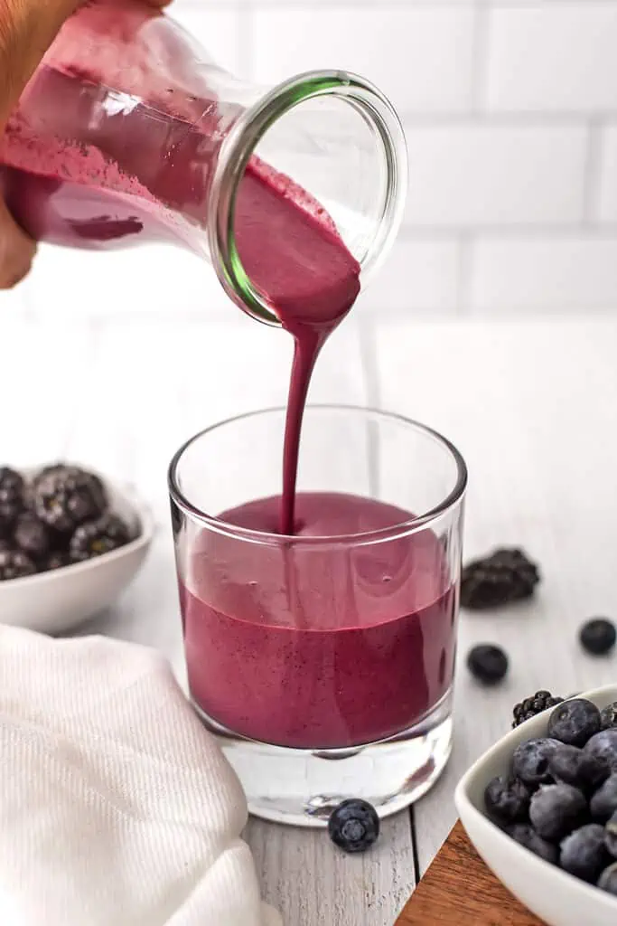 Blackberry blueberry smoothie being poured into a glass after being blended.