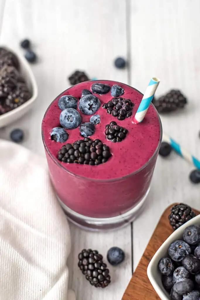 Blueberry and blackberry smoothie on a white table with fresh blueberries and blackberries in white ramekins.