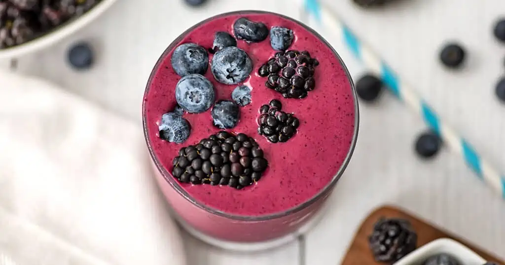 Blueberry and blackberry smoothie in a small glass with topping of fresh blueberries and blackberries.