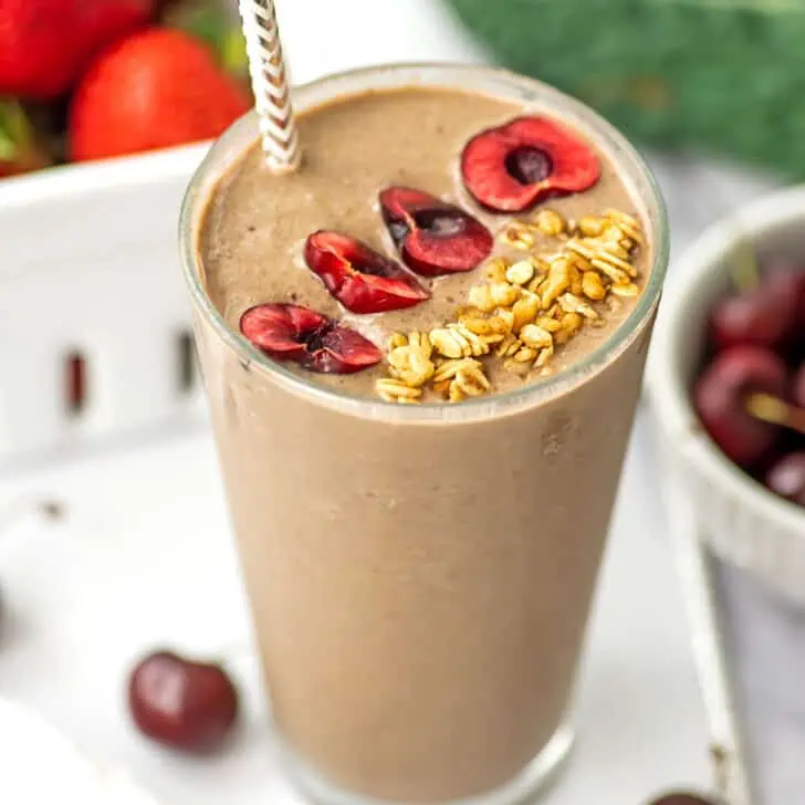 Cherry kale smoothie in a tall glass with sliced cherries and granola on top.