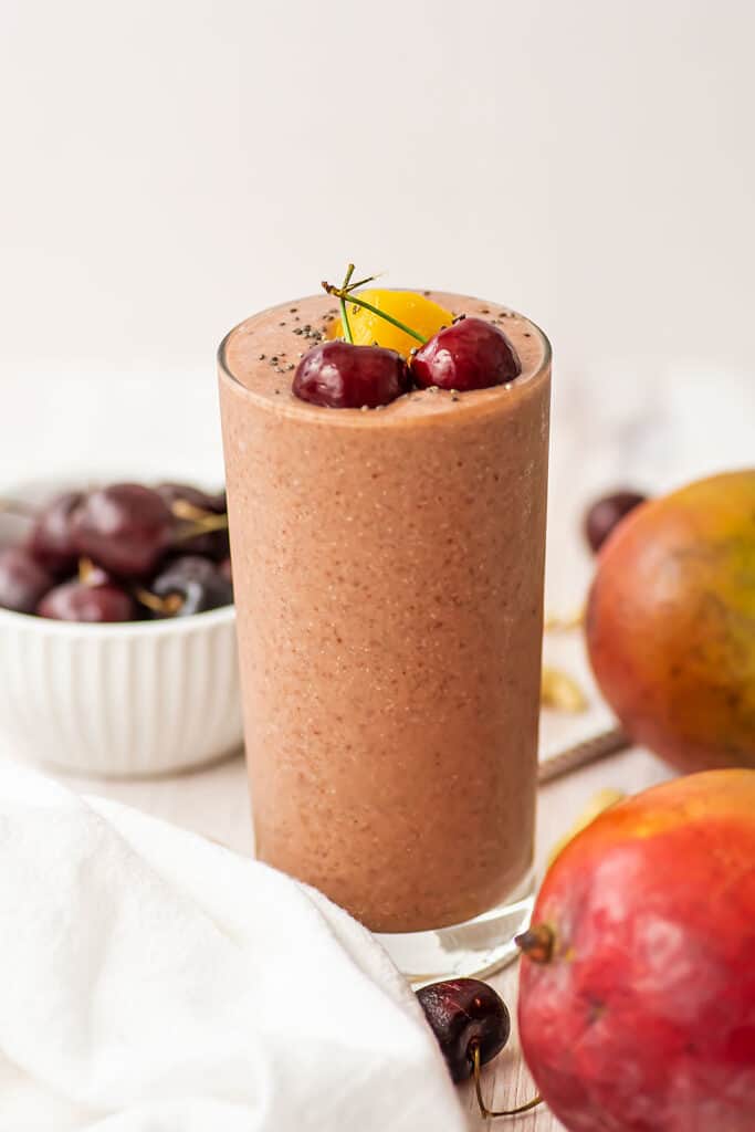 Cherry mango smoothie in a tall glass with fresh cherries on top.