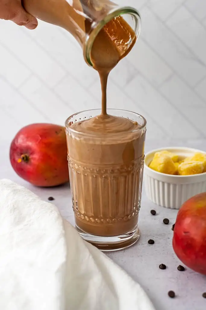 Chocolate mango protein smoothie being poured into a glass.