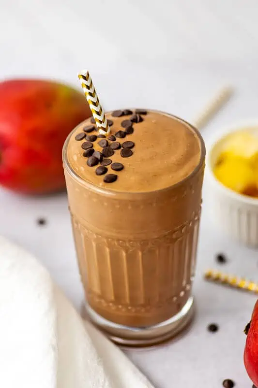 Chocolate mango smoothie in a glass with a straw and cacao nibs on top.