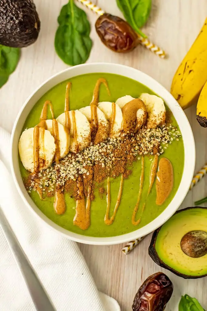 Date avocado smoothie bowl with sliced banana, granola, cinnamon and nut butter drizzled on top.
