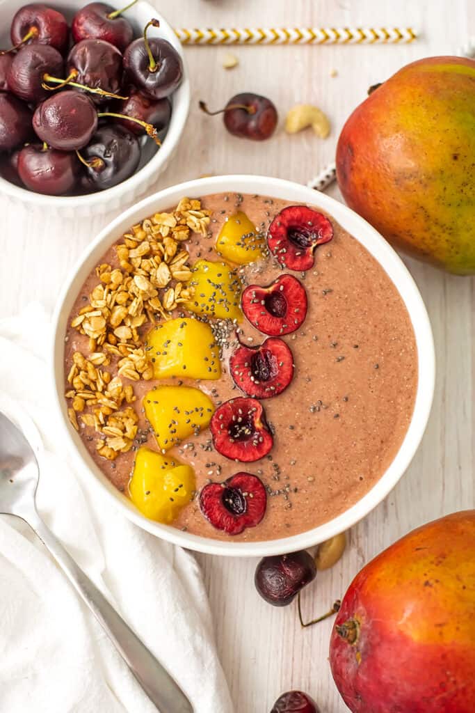 Mango cherry smoothie bowl with mango chunks, sliced cherries and granola as toppings.