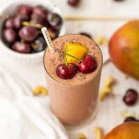 Mango cherry smoothie with a bowl of cherries in the background.