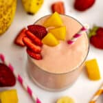 Mango strawberry banana smoothie topped with sliced strawberries and mango chunks.