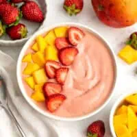 Mango strawberry smoothie bowl topped with sliced fruit.