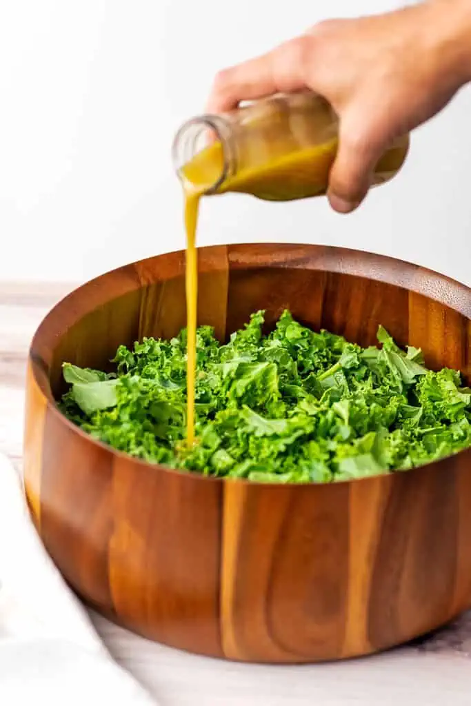 Kale salad in wood bowl with maple dijon dressing poured over the kale.