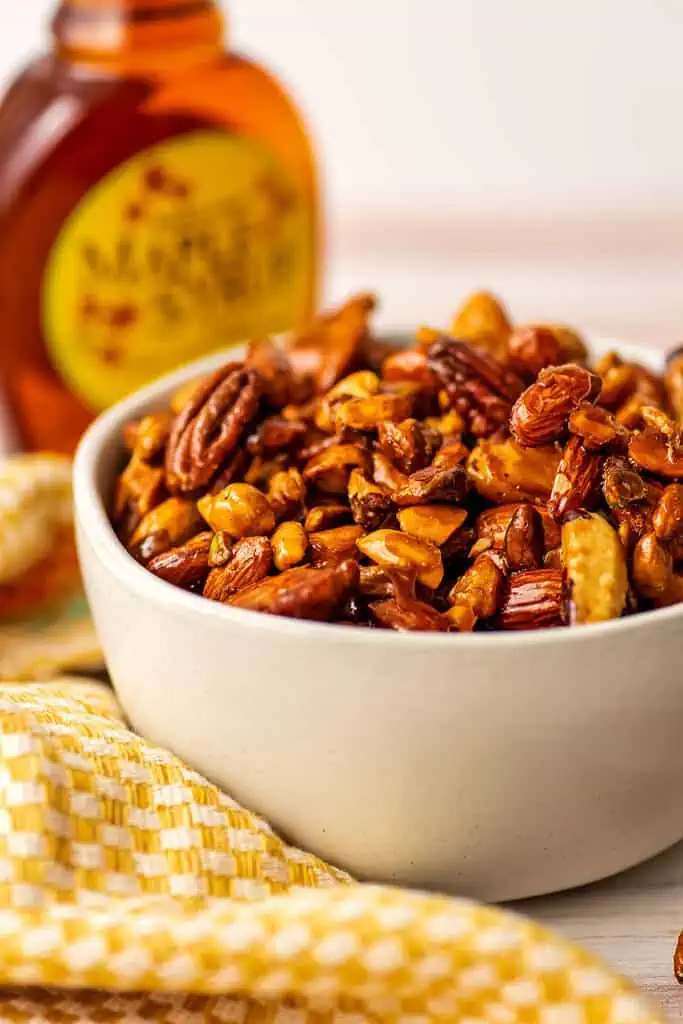 Maple nuts in a bowl with a bottle of male syrup in the background.