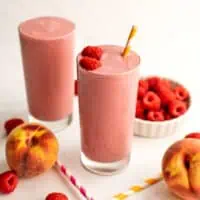 Peach raspberry smoothie with a bowl of raspberries in the background.