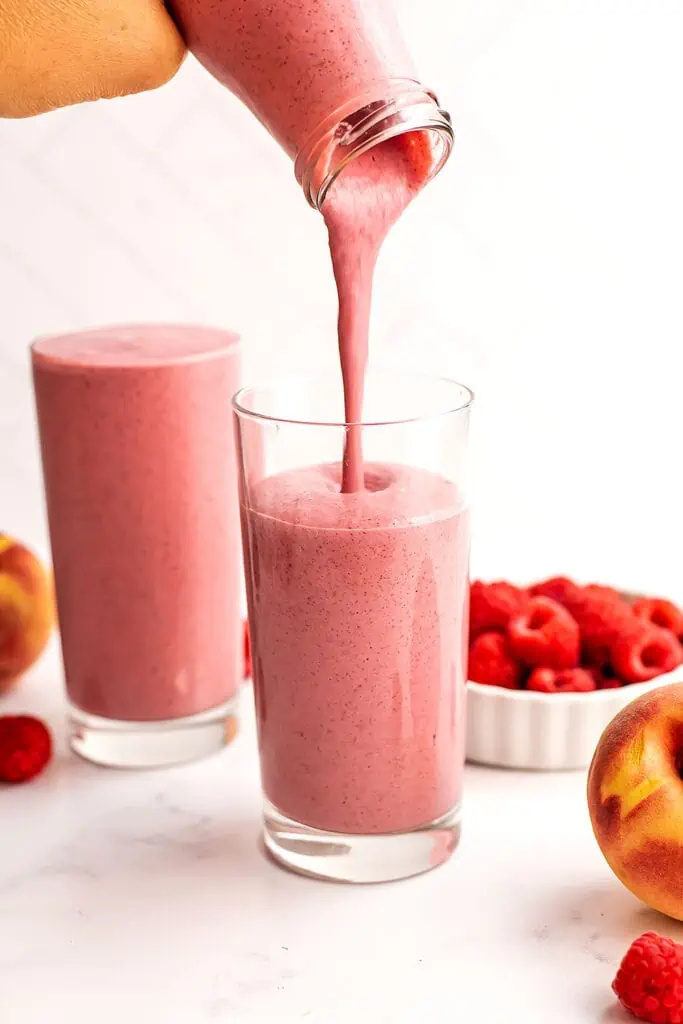Peach and raspberry smoothie with yogurt being poured into a glass.