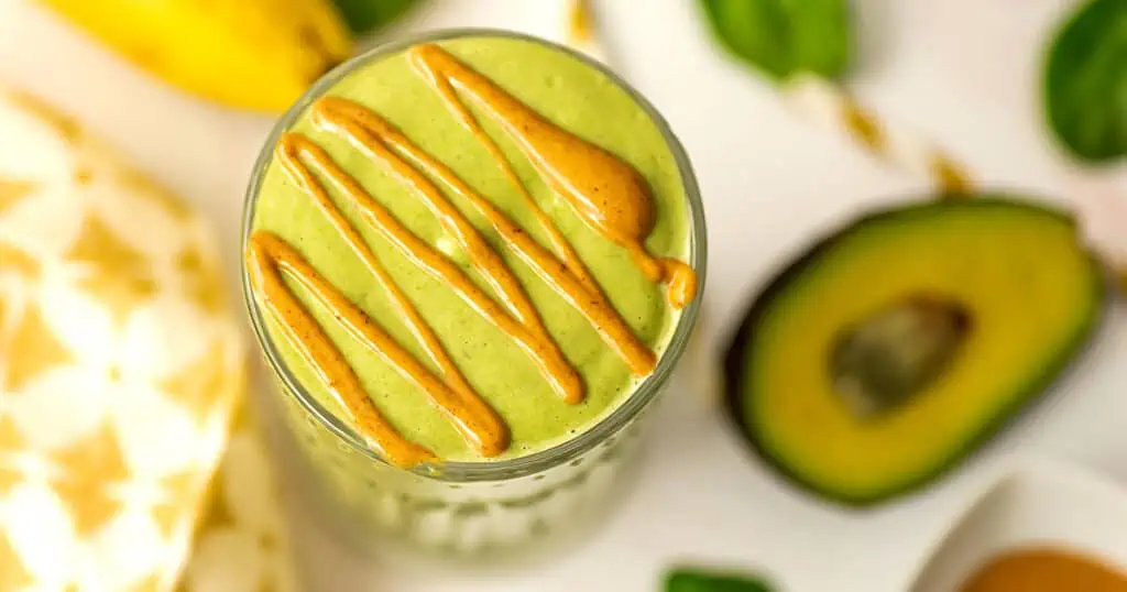 Peanut butter banana avocado smoothie in a glass with nut butter drizzle on top.