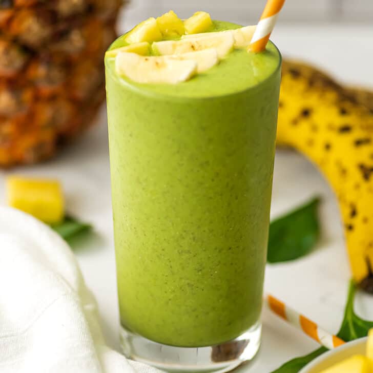 Pineapple banana spinach smoothie with pineapple slices on top and a straw.