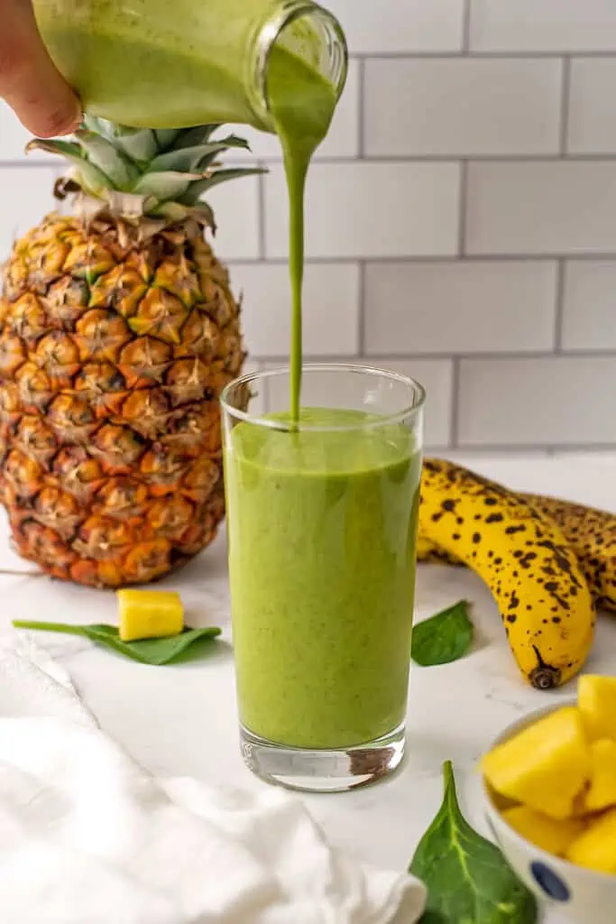 Pineapple banana spinach smoothie being poured into a glass.