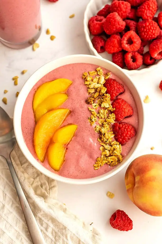 Raspberry peach smoothie bowl with fresh peaches, raspberries and granola toppings.