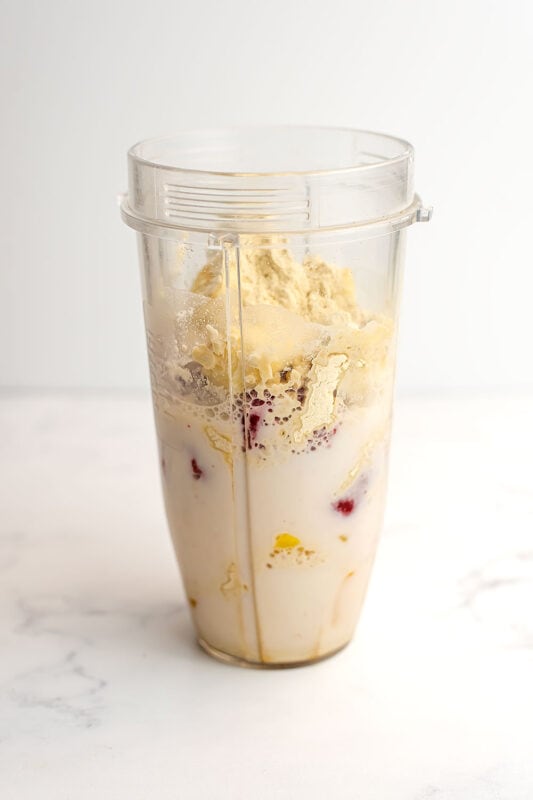 Strawberry mango banana smoothie ingredients in a blender cup before being blended.