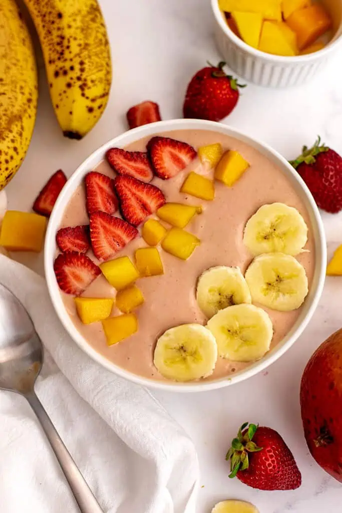 Strawberry mango banana smoothie in a bowl with sliced bananas, strawberries and mangos on top.