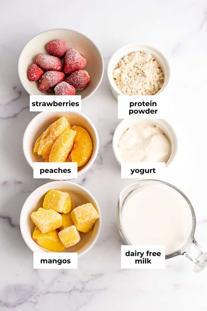 Strawberry mango peach smoothie ingredients in white ramekins.