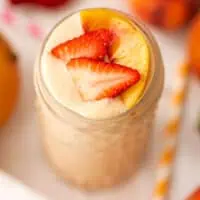 Strawberry mango peach smoothie in a tall glass topped with sliced strawberries.