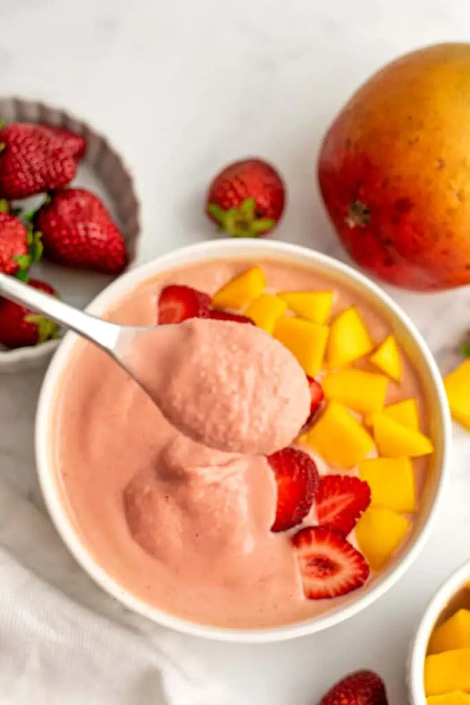 Strawberry mango smoothie bowl with a smoothie bowl of smoothie being scooped out of it.