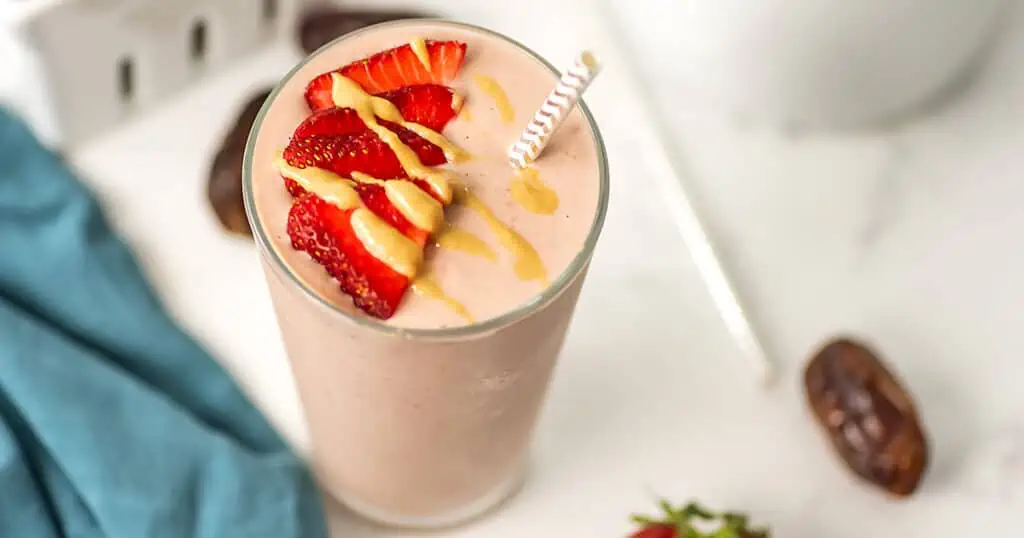 Strawberry smoothie no banana with tahini drizzle on top on a white table.