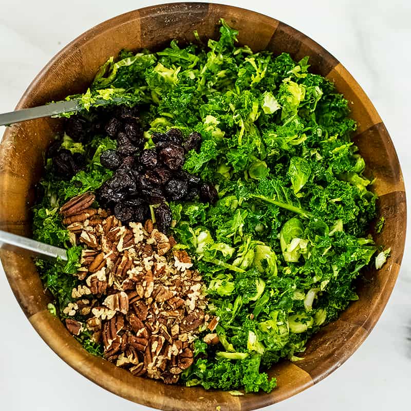 Kale, brussel sprouts, cranberries and chopped pecans in salad bowl.