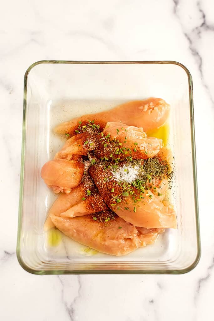 Chicken tenders with spices and olive oil in a glass container.