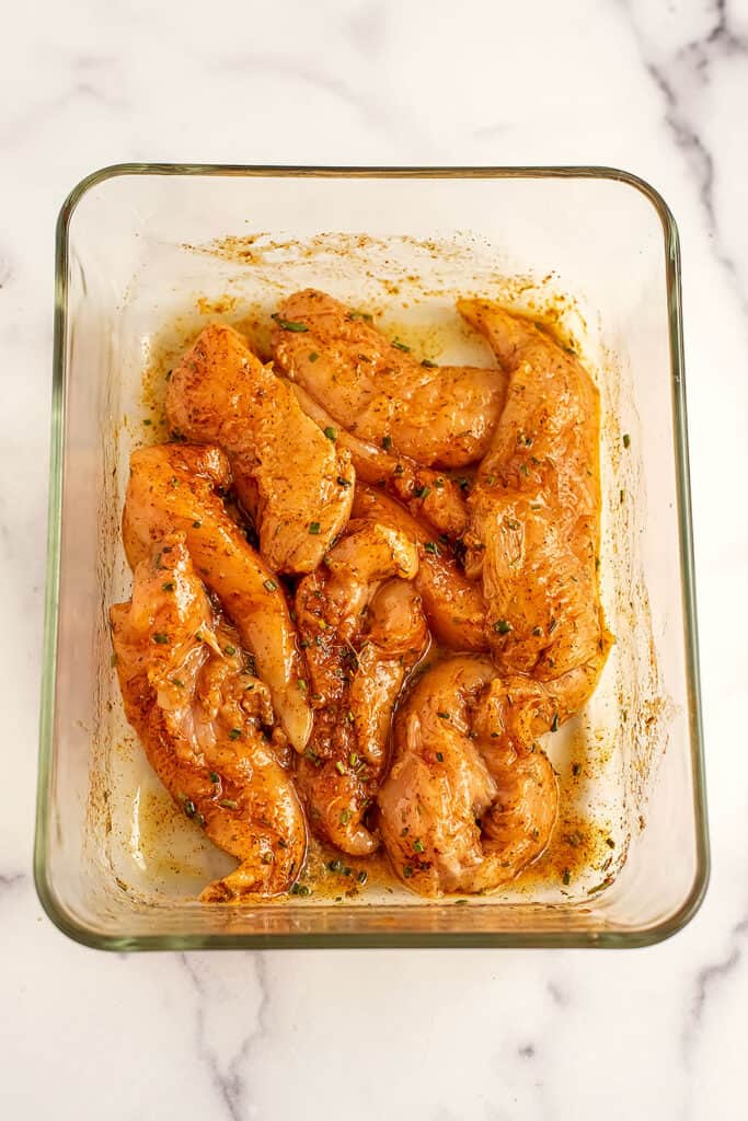 Chicken tenders coated with spices in a glass container.