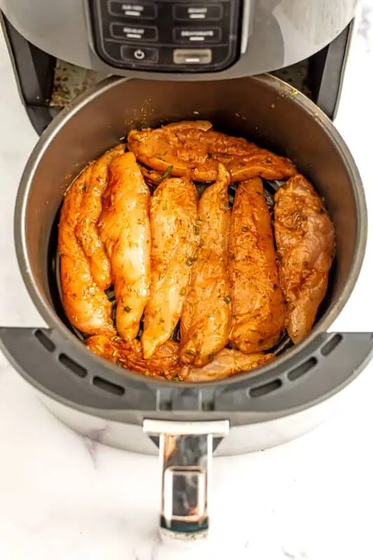 Raw chicken tenders in air fryer basket before cooking.