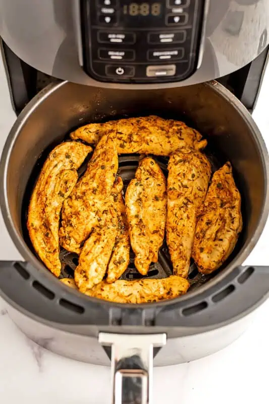 Fully cooked chicken tenders in air fryer basket.
