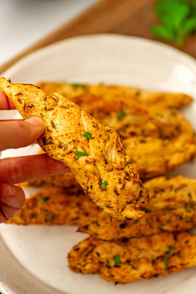 Hand holding a grilled air fryer chicken tender over the plate.