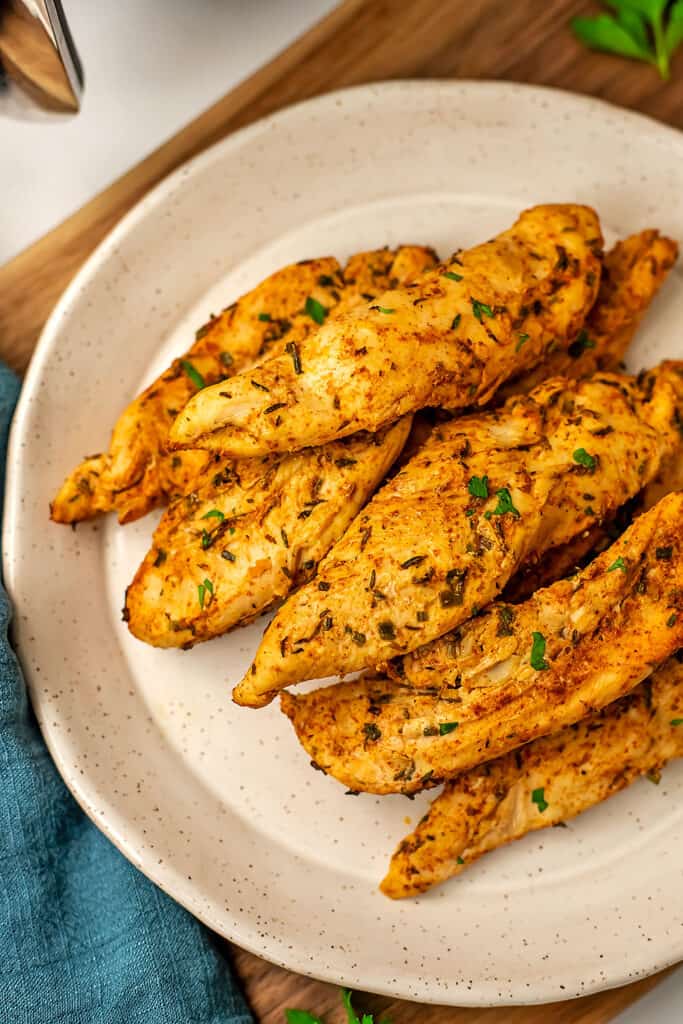 Air fryer chicken tenders stacked on a white plate.