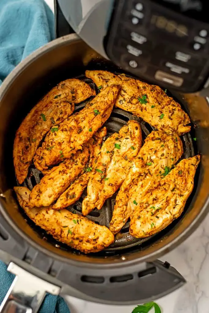 Grilled chicken tenders in an air fryer basket with blue napkin on the side.