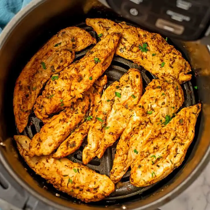 Grilled chicken tenders in an air fryer basket with blue napkin on the side.
