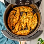 Chicken tenders in air fryer basket with a blue napkin on the side.