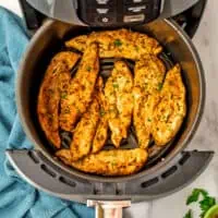 Chicken tenders in air fryer basket with a blue napkin on the side.
