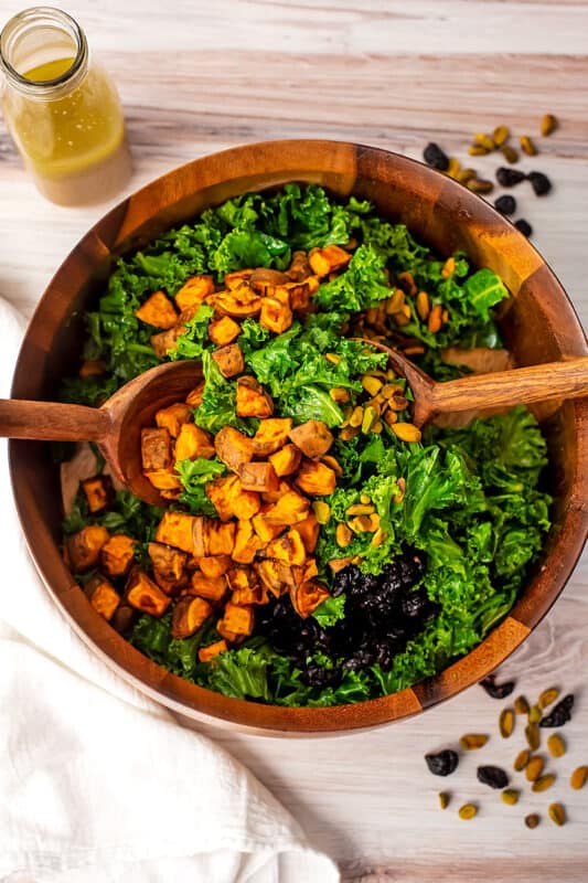 Wooden salad forks mixing up bowl of sweet potato kale salad.