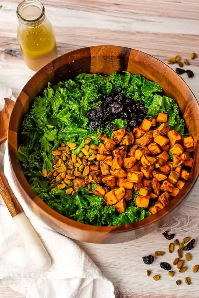 Ingredients for kale and sweet potato salad in wood bowl before mixing.