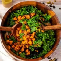 Kale sweet potato salad in wood bowl with wood salad tongs resting in bowl.